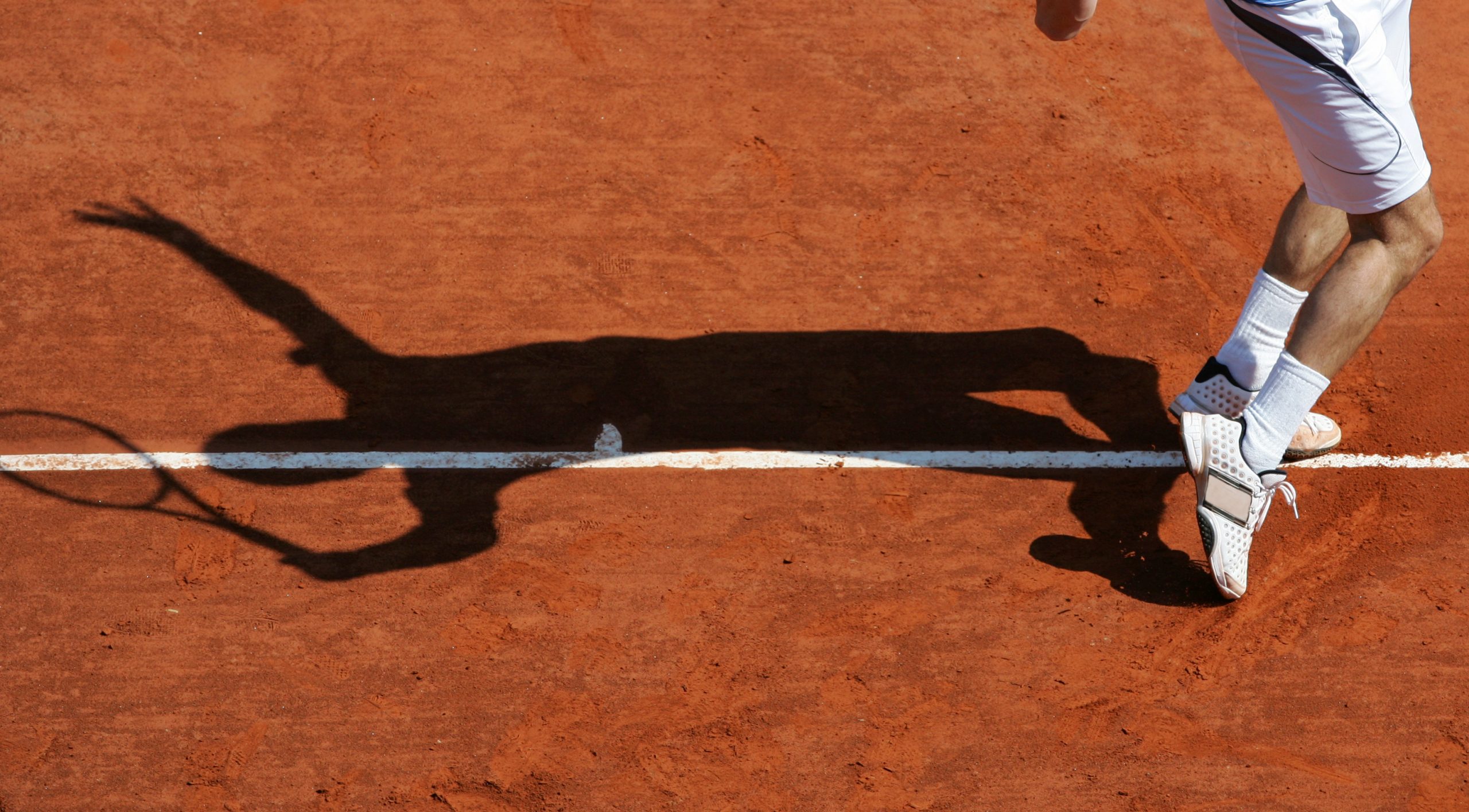 The shadow of a man playing tennis on a court.